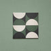 Single tile image showing the Geometry Circulo 20x20cm geometric patterned tile with green, black, and cream semicircle motifs, photographed against a soft green textured background.