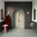 Bathroom featuring Geometry Hourglass 20cm x 20cm patterned floor tiles, paired with dark fluted wall tiles, an arched walk-in shower, brushed brass fittings, a floating vanity and striking geometric green feature tiles.