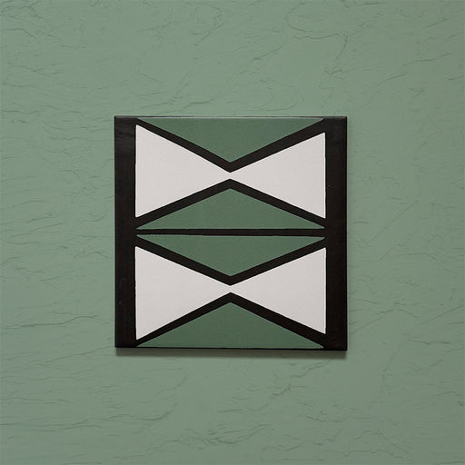 Single tile image showing the Geometry Hourglass 20x20cm patterned tile with alternating green and cream hourglass shapes outlined in charcoal, photographed against a textured sage-green background.
