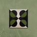 Single tile image showing the Geometry Illusion Verde Noir 20x20cm geometric patterned tile with green and black semicircles and cream corner details, photographed against a soft mottled green background.