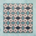 Group image showing multiple Geometry Iris 20x20cm patterned tiles arranged in a repeating layout, featuring an intricate geometric design in teal, navy, terracotta-red, and cream, photographed against a soft mottled aqua background.
