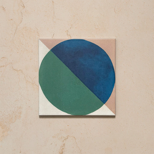 Single tile image showing the Geometry Ocean 20x20cm geometric patterned tile with blue and green semicircles on a sand and white background, photographed against a neutral stone surface.