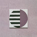 Single tile image showing the Geometry Seritina 20x20cm patterned tile with green horizontal stripes and a mauve semicircle on a cream base, photographed against a textured pink background.