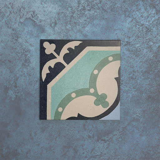 Single Europa Gothenberg 20x20cm Victorian Moroccan style tile displayed against a textured blue background, showcasing a geometric corner pattern in blue, mint green and cream tones in a close-up product setting.
