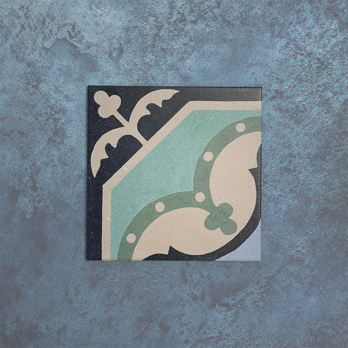 Single Europa Gothenberg 20x20cm Victorian Moroccan style tile displayed against a textured blue background, showcasing a geometric corner pattern in blue, mint green and cream tones in a close-up product setting.