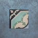 Single Europa Gothenberg 20x20cm Victorian Moroccan style tile displayed against a textured blue background, showcasing a geometric corner pattern in blue, mint green and cream tones in a close-up product setting.