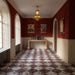 Interior featuring Grand Bazaar Violetta Matt and Grand Bazaar Levant Rouge marble-effect chequerboard floor tiles, combining rich burgundy, deep violet and white tones in a striking geometric layout. Styled with warm red walls, decorative artwork, elegant lighting and classic architectural details to create a luxurious, maximalist-inspired space full of character.