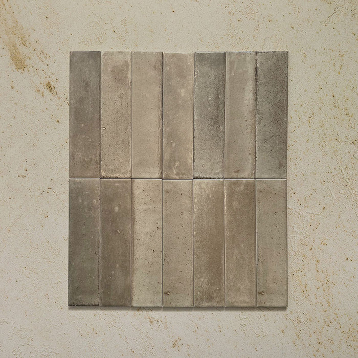 Group of Izmir Brick Sage Green Gloss 6x25cm ceramic tiles displayed on a textured beige surface, showing natural shade variation and a reflective glossy finish.