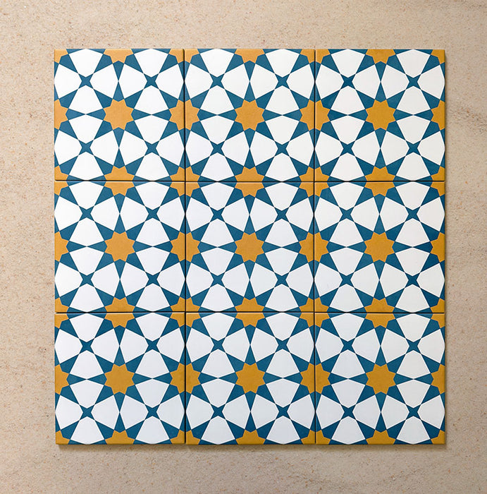 Close-up of multiple Agraba Sunshine 20x20cm Moroccan-style ceramic tiles arranged in a grid, showcasing a vibrant geometric star pattern in blue, mustard yellow, and white on a neutral sandy background.