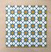 Close-up of multiple Agraba Sunshine 20x20cm Moroccan-style ceramic tiles arranged in a grid, showcasing a vibrant geometric star pattern in blue, mustard yellow, and white on a neutral sandy background.