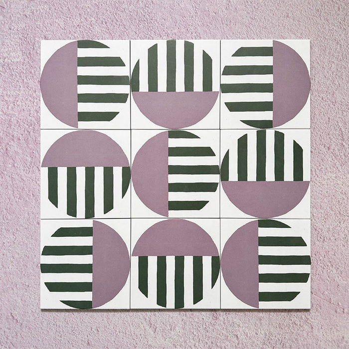 Group image showing multiple Geometry Seritina 20x20cm patterned tiles arranged in a repeating layout, featuring green striped semicircles and mauve solid semicircles on a cream base, photographed against a textured pink background.