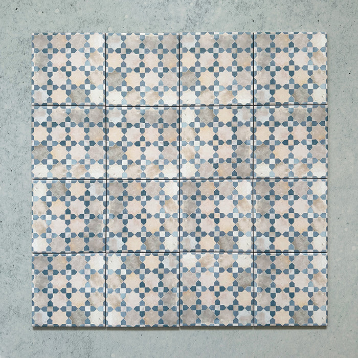 Group of Bedouin Mequinez Blue Moroccan-style wall and floor tiles, each 15x15cm, arranged in a repeating geometric pattern of soft blues, creams, and taupe tones on a light textured background, showcasing the overall design effect.
