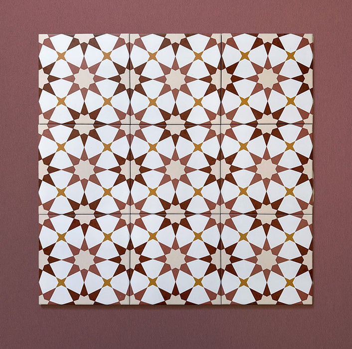 Close-up of multiple Agraba Cotto 20x20cm Moroccan-style ceramic tiles arranged in a grid, showing a geometric star pattern in terracotta, beige, mustard, and white tones on a warm burgundy background.