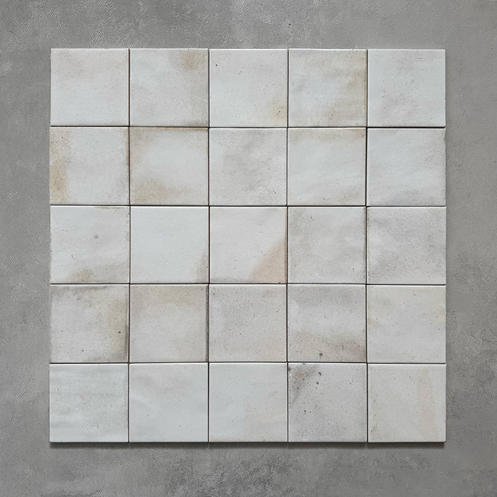 Group of Beijing White 10x10cm Moroccan square tiles arranged on a grey background, featuring soft tonal variation, subtle glaze differences, and handmade-style edges that create a natural, artisanal look.