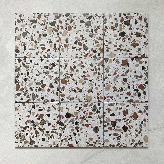 Flatlay featuring a group of Dino Terrazzo Blanco Drops 20x20cm terrazzo-style ceramic tiles, displaying a white background with large stone-effect chips in brown, terracotta, and grey tones.