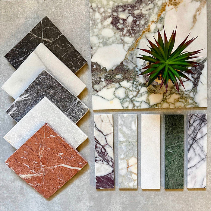 Flat lay featuring Fitzrovia Lilac 5 x 20cm honed natural marble tiles alongside coordinating marble finishes, showcasing a soft white base with lilac-grey veining, complemented by richer tones and textures for a layered, design-led palette.
