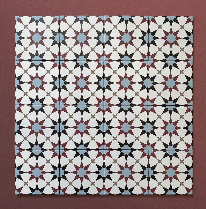 Close-up of multiple Agraba Mini Atlas 15x15cm Moroccan-style ceramic tiles arranged in a grid, showcasing a colourful geometric star pattern in blue, terracotta, black, and white on a warm burgundy background.
