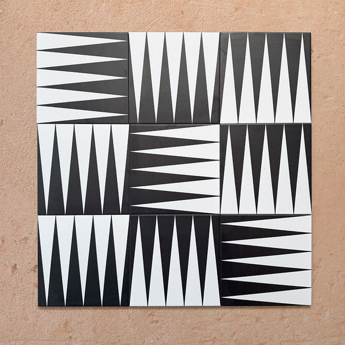 Group of Alhambra Tavla 20x20cm Moroccan tiles displaying a striking black and white triangular geometric pattern, arranged to create a bold, dynamic layout on a warm textured background.