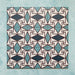 Group image showing multiple Geometry Iris 20x20cm patterned tiles arranged in a repeating layout, featuring an intricate geometric design in teal, navy, terracotta-red, and cream, photographed against a soft mottled aqua background.