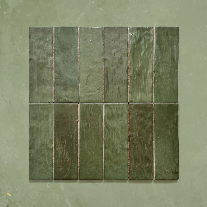 Zellij Botanical Green brick tiles, 6.5cm x 20cm, Moroccan style glazed ceramic tiles in rich botanical green tones with natural tonal variation, glossy finish, and softly uneven handcrafted surface, arranged as a grouped tile layout on a muted green background.