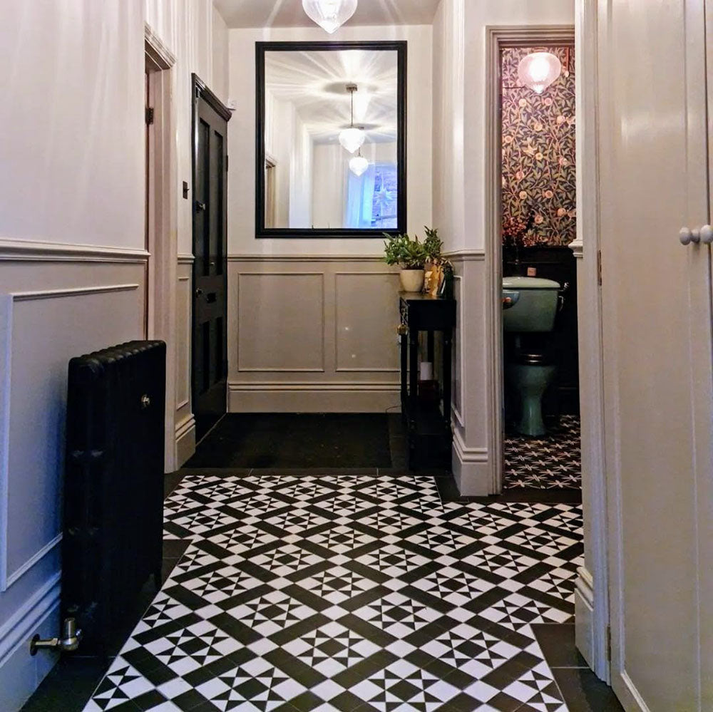 Hallway featuring Sloane Square Black and White 25x25cm Victorian-style ceramic floor tiles, laid in a classic geometric pattern with monochrome tones, styled with paneled walls, a black radiator, and a large framed mirror.