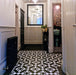 Hallway featuring Sloane Square Black and White 25x25cm Victorian-style ceramic floor tiles, laid in a classic geometric pattern with monochrome tones, styled with paneled walls, a black radiator, and a large framed mirror.