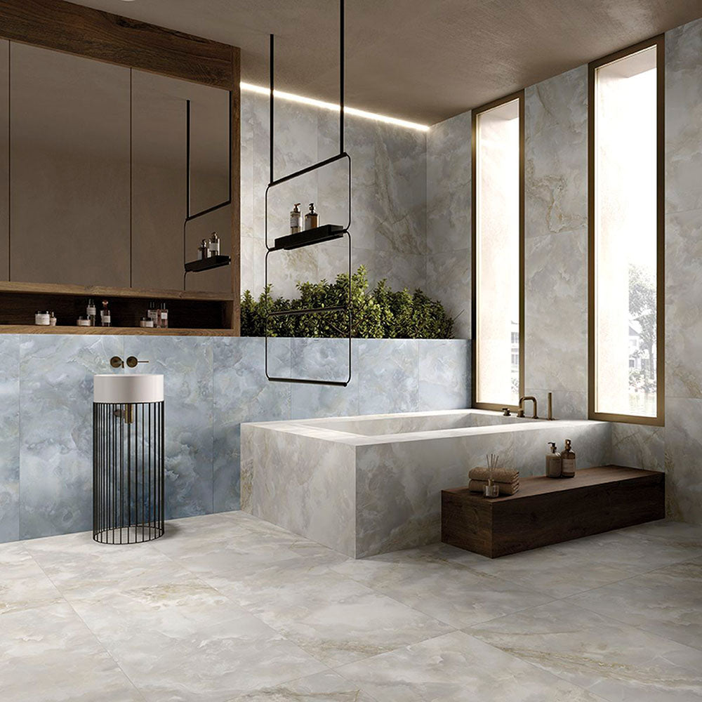 Contemporary luxury bathroom featuring Hashim Blue Honed Matt Onyx porcelain tiles on the walls and bath surround. The soft blue onyx-effect veining pairs beautifully with warm wood cabinetry, black accents and large-format stone effect floor tiles to create a calm, spa-inspired space.