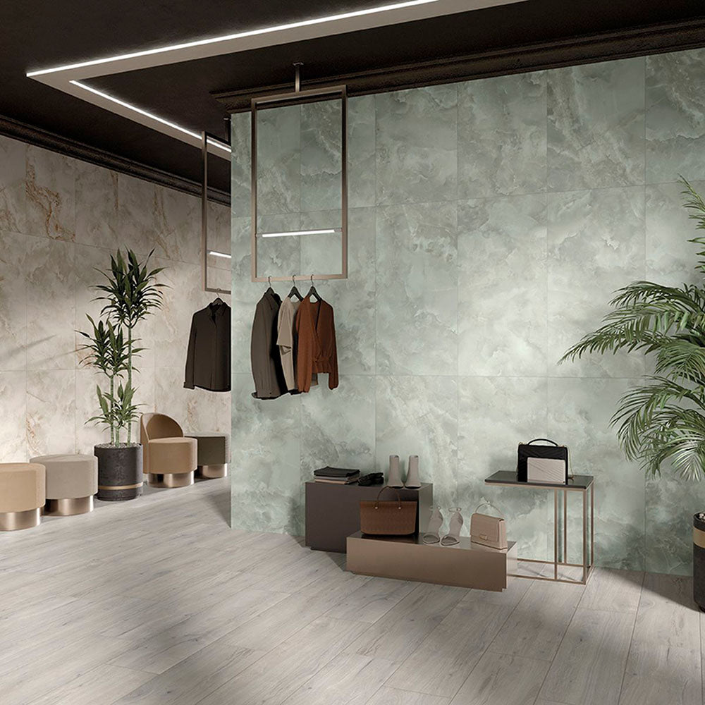 Contemporary retail interior featuring Hashim Green Honed Matt Onyx 60x60cm porcelain tiles on a large feature wall. The soft green onyx effect with flowing natural veining creates a luxurious backdrop, complemented by pale wood effect flooring, warm neutral furnishings and modern display fixtures.