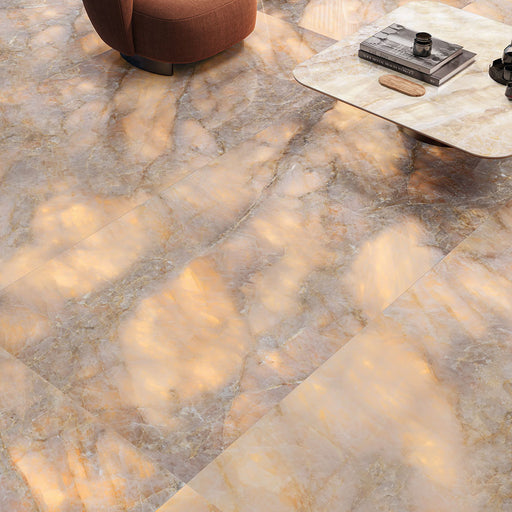 Living area featuring Illuminati Precious Stone Amber 60 × 120cm polished porcelain floor tiles, showcasing warm amber and taupe gemstone-inspired veining, paired with soft contemporary furnishings and a marble-effect coffee table.