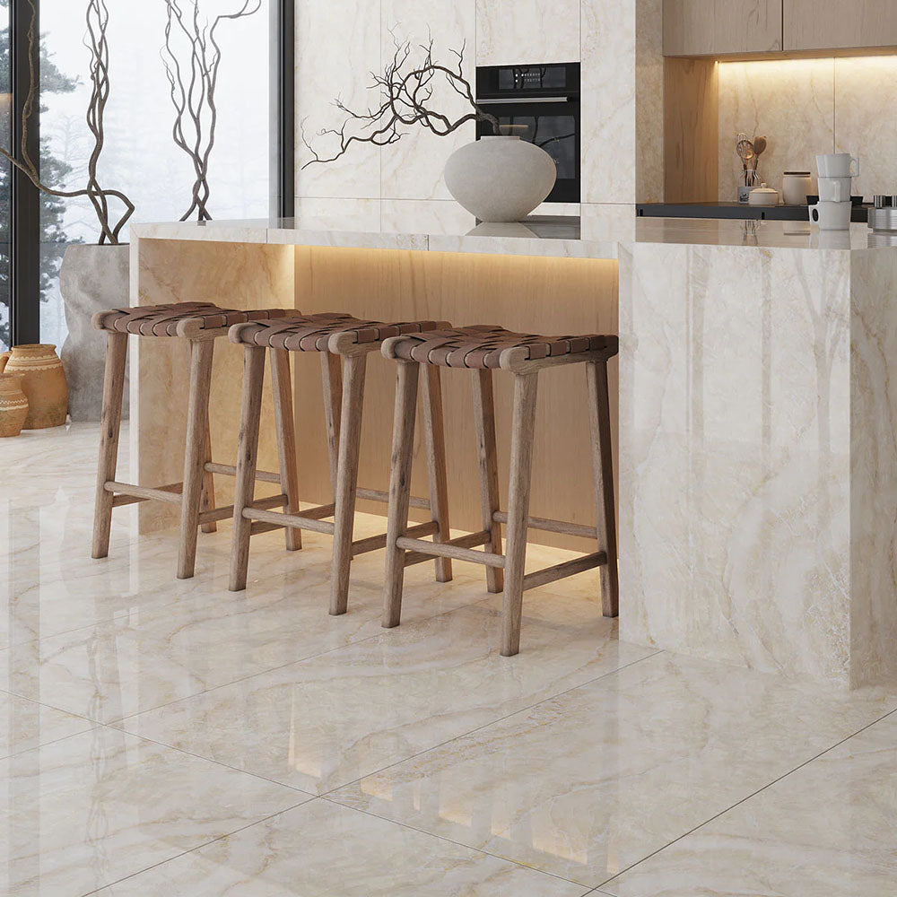 Contemporary kitchen featuring Illuminati Precious Stone Ivory 60 × 120cm polished porcelain floor and wall tiles, showcasing soft ivory and cream gemstone-inspired veining, paired with warm wood bar stools and minimalist cabinetry.