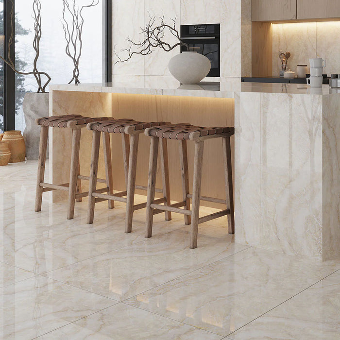 Contemporary kitchen featuring Illuminati Precious Stone Ivory 60 × 120cm polished porcelain floor and wall tiles, showcasing soft ivory and cream gemstone-inspired veining, paired with warm wood bar stools and minimalist cabinetry.