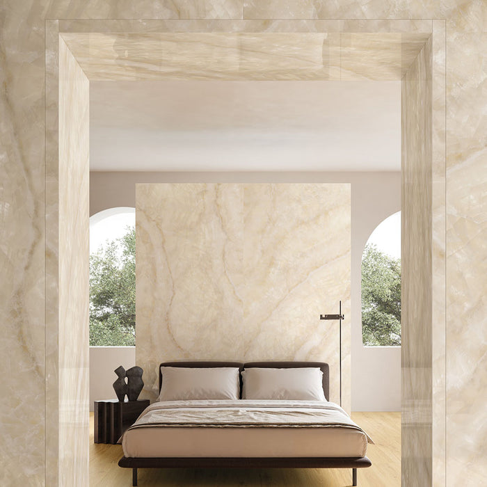 Minimalist bedroom featuring Illuminati Precious Stone Ivory 60 × 120cm polished porcelain wall tiles, showcasing soft ivory and cream gemstone-inspired veining, paired with warm wood flooring, neutral furnishings, and arched architectural details.