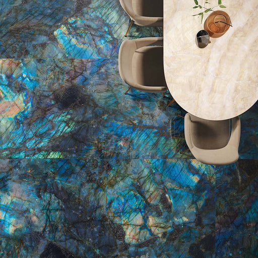 Dining area featuring Illuminati Precious Stone Labradorite 60 × 120cm polished porcelain floor tiles, showcasing dramatic blue and charcoal gemstone-inspired veining, paired with curved upholstered dining chairs and a soft neutral dining table.
