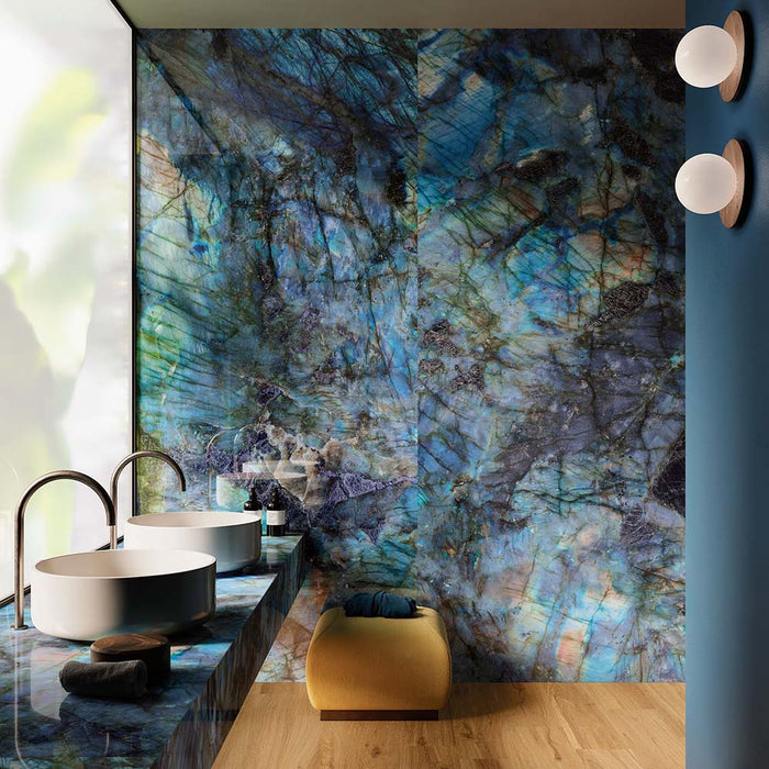 Luxury bathroom featuring Illuminati Precious Stone Labradorite 60 × 120cm polished porcelain wall tiles, showcasing striking blue gemstone-inspired veining, paired with twin vessel basins, dark brass fittings, and warm wood flooring.