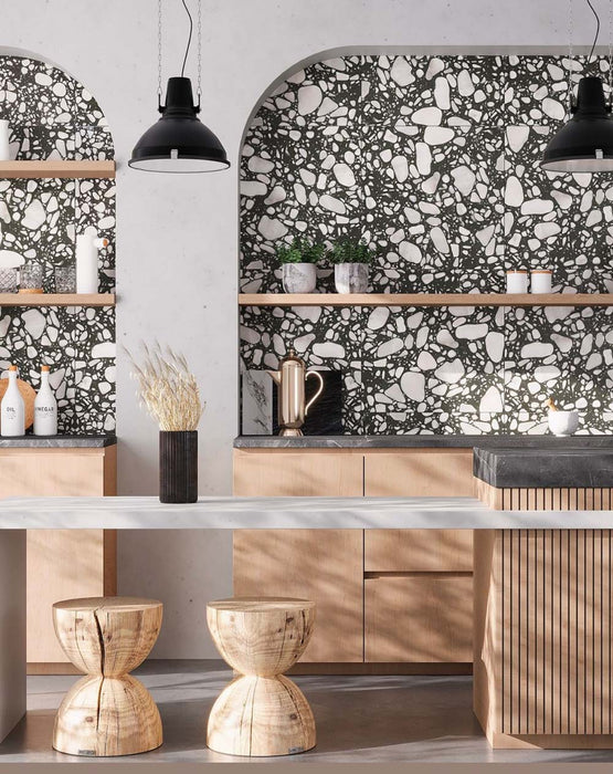Kitchen setting featuring Noventa Terrazzo Nero 59x59cm matt porcelain wall and floor tiles, showcasing a bold terrazzo effect with contrasting white stone fragments set against a deep black base, installed within arched alcoves and paired with warm wood cabinetry and soft neutral surfaces for a refined, architectural finish.