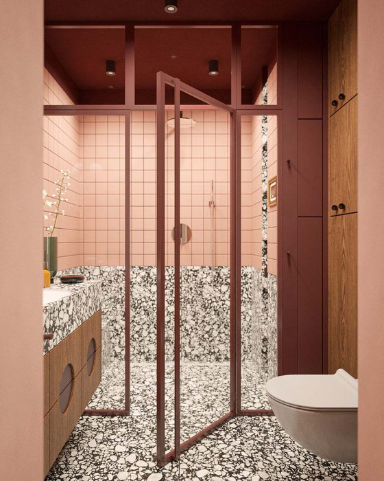 Bathroom setting featuring Noventa Terrazzo Nero 59x118cm matt porcelain wall and floor tiles, showcasing a bold terrazzo effect with contrasting white stone fragments set against a deep black base, used across both floor and lower wall sections, paired with soft blush wall tiles, warm wood cabinetry and tonal framing for a refined, design-led finish.