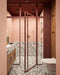 Bathroom setting featuring Noventa Terrazzo Nero 59x118cm matt porcelain wall and floor tiles, showcasing a bold terrazzo effect with contrasting white stone fragments set against a deep black base, used across both floor and lower wall sections, paired with soft blush wall tiles, warm wood cabinetry and tonal framing for a refined, design-led finish.