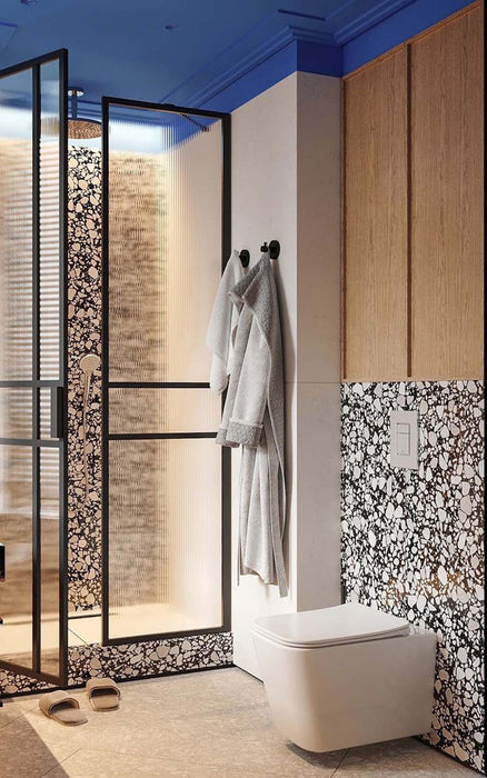 Bathroom setting featuring Noventa Terrazzo Nero 59x59cm matt porcelain wall and floor tiles, showcasing a bold terrazzo effect with crisp white stone fragments set against a deep black base, used as a striking feature wall and shower detail, paired with warm wood cabinetry, soft neutral tones and black-framed glass for a contemporary, design-led finish.