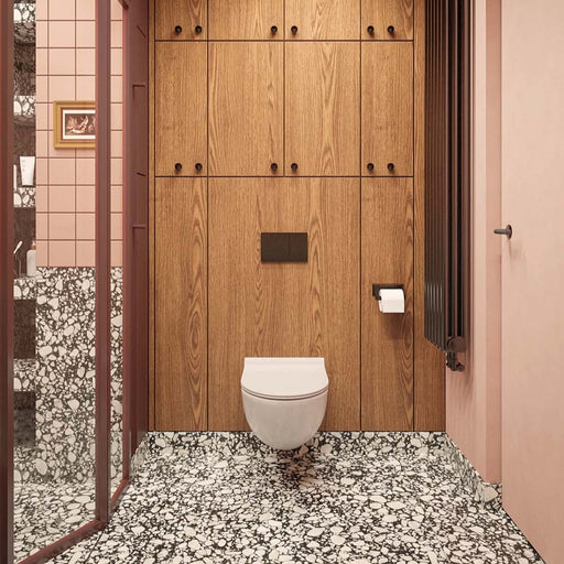 Bathroom setting featuring Noventa Terrazzo Nero 59x118cm matt porcelain wall and floor tiles, showcasing a bold terrazzo effect with contrasting white stone fragments set against a deep black base, used across both floor and lower wall sections, paired with soft blush wall tiles, warm wood cabinetry and tonal framing for a refined, design-led finish.
