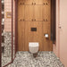 Bathroom setting featuring Noventa Terrazzo Nero 59x118cm matt porcelain wall and floor tiles, showcasing a bold terrazzo effect with contrasting white stone fragments set against a deep black base, used across both floor and lower wall sections, paired with soft blush wall tiles, warm wood cabinetry and tonal framing for a refined, design-led finish.