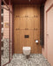 Bathroom setting featuring Noventa Terrazzo Nero 59x118cm matt porcelain wall and floor tiles, showcasing a bold terrazzo effect with contrasting white stone fragments set against a deep black base, used across both floor and lower wall sections, paired with soft blush wall tiles, warm wood cabinetry and tonal framing for a refined, design-led finish.