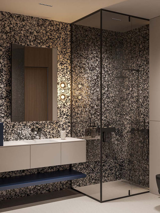 Bathroom setting featuring Noventa Terrazzo Nero 59x59cm matt porcelain wall and floor tiles, showcasing a bold terrazzo effect with contrasting white stone fragments set against a deep black base, used across full-height walls and within the shower enclosure, paired with clean-lined cabinetry, soft lighting and black accents for a refined, architectural finish.