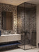 Bathroom setting featuring Noventa Terrazzo Nero 59x59cm matt porcelain wall and floor tiles, showcasing a bold terrazzo effect with contrasting white stone fragments set against a deep black base, used across full-height walls and within the shower enclosure, paired with clean-lined cabinetry, soft lighting and black accents for a refined, architectural finish.