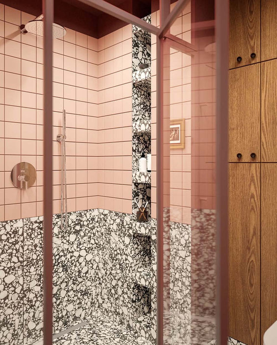 Bathroom setting featuring Noventa Terrazzo Nero 59x118cm matt porcelain wall and floor tiles, showcasing a bold terrazzo effect with contrasting white stone fragments set against a deep black base, used across both floor and lower wall sections, paired with soft blush wall tiles, warm wood cabinetry and tonal framing for a refined, design-led finish.