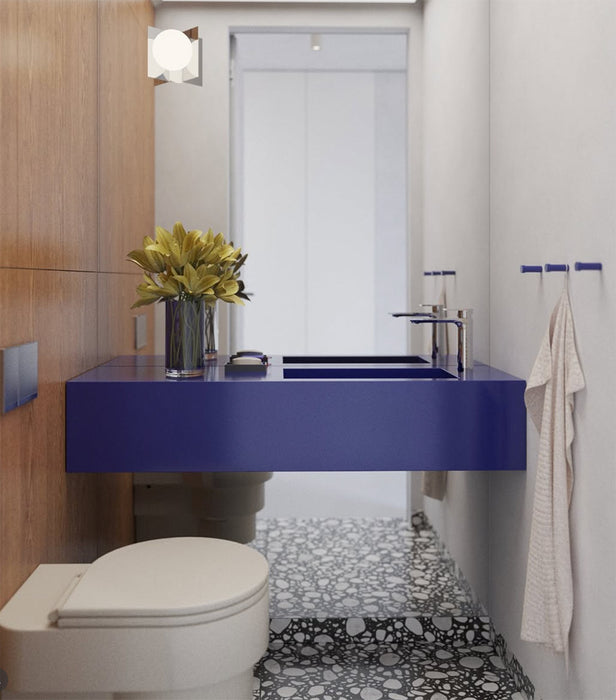 Bathroom setting featuring Noventa Terrazzo Nero 59x59cm matt porcelain wall and floor tiles, showcasing a bold terrazzo effect with crisp white stone fragments set against a deep black base, carried across both floor and stepped detailing, paired with warm wood panelling and a striking cobalt vanity for a contemporary, design-led finish.