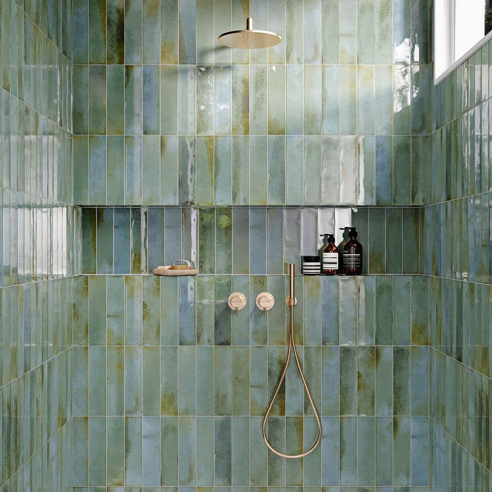 Contemporary shower featuring Izmir Brick Celadon Green Gloss 6x25cm ceramic wall tiles, styled with brushed brass fixtures, built-in shelving with amber bottles, and natural light reflecting on the glossy surface.