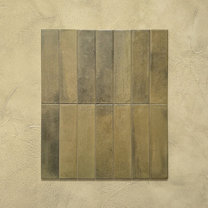 Group of Izmir Brick Daisy Green Gloss 6x25cm ceramic tiles displayed on a textured beige background, highlighting the natural colour variation, glossy finish, and handcrafted look.