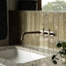 Bathroom featuring Izmir Sage Green gloss brick tiles in a 6 × 25cm ceramic format, installed vertically to create a soft, elongated look, with subtle tonal variation and a high-gloss finish that reflects natural light, paired with warm wood panelling, terrazzo surfaces and minimalist brass fittings for a calm, spa-inspired interior.