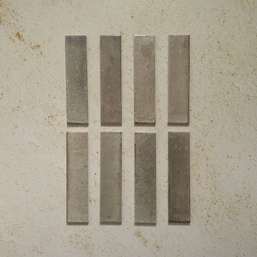 Eight Izmir Brick Sage Green Gloss 6x25cm ceramic tiles displayed on a textured beige background, showing gentle tonal variation and a soft glossy finish.