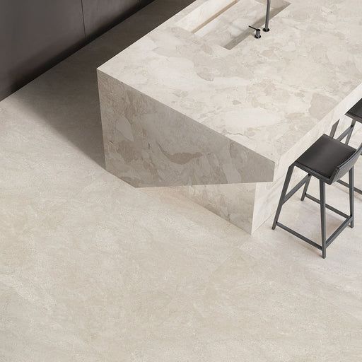 Contemporary kitchen featuring Jeddah Avorio Neutra Stone 30x60cm stone-effect wall and floor tiles, showcasing warm ivory and beige tones, paired with a matching waterfall island, black bar stools and minimalist finishes.